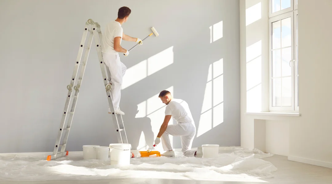 Deux hommes peignent une pièce en blanc dans le cadre d'une rénovation domiciliaire.