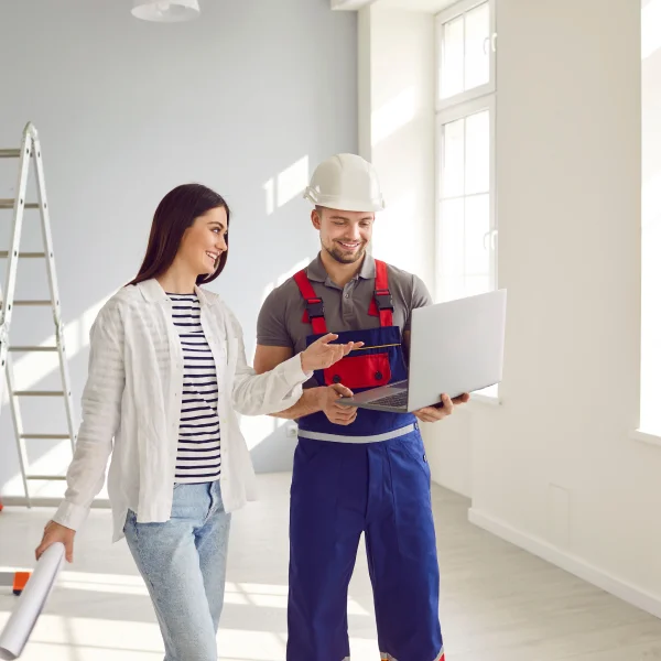 Dans un bureau, un homme et une femme se concentrent sur un ordinateur portable, avec des détails de rénovation intérieure visibles.