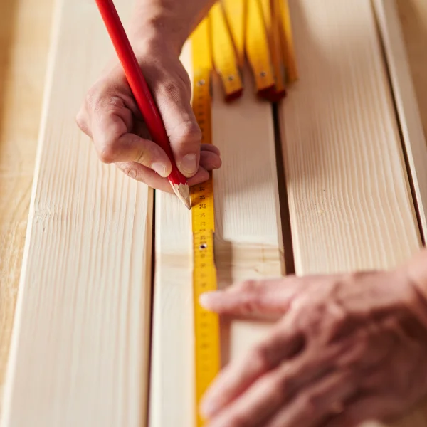 Une personne mesure la longueur d'un morceau de bois avec une règle, en lien avec des portes sur mesure.